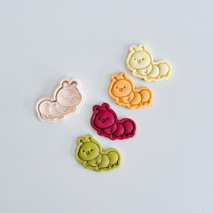 Può includere: Una collezione di formine per biscotti a forma di bruco colorato. Le formine sono nelle tonalità di rosa, rosso, arancione, giallo e verde. Ogni formina ha un contorno dettagliato e un design carino e a cartoni animati, perfetto per dolcetti a tema.