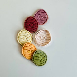 Pu&ograve; includere: Sei stampini per biscotti a forma di favo con un cuore al centro. Gli stampini sono di vari colori, tra cui rosa, rosso, giallo, arancione e verde.