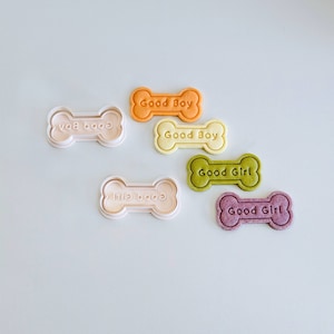 May include: Six dog bone-shaped cookies, two orange, two yellow, and two purple, with the words "Good Boy" and "Good Girl" embossed on them.  There are also two white plastic dog bone cookie cutters.