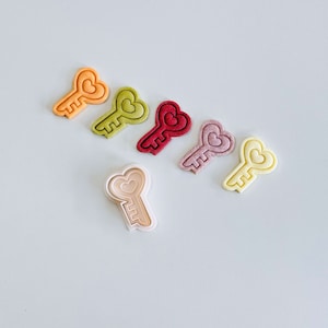 Op de afbeelding: Zes hartvormige koekjesvormen in verschillende kleuren, waaronder oranje, geel, groen, rood, roze en crème.