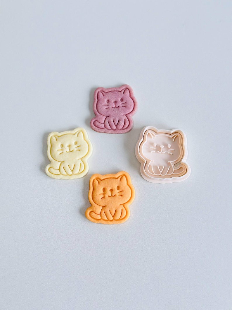 Puede incluir: Cuatro cortadores de galletas con forma de gato en amarillo, rosa, naranja y morado. Cada cortador presenta un dise&ntilde;o sencillo de dibujos animados de un gato sentado con una cara sonriente. Ideal para hornear galletas tem&aacute;ticas.