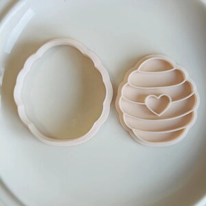 Pu&ograve; includere: Due stampini per biscotti in plastica, uno a forma di favo con un cuore al centro e l'altro a forma di cerchio.