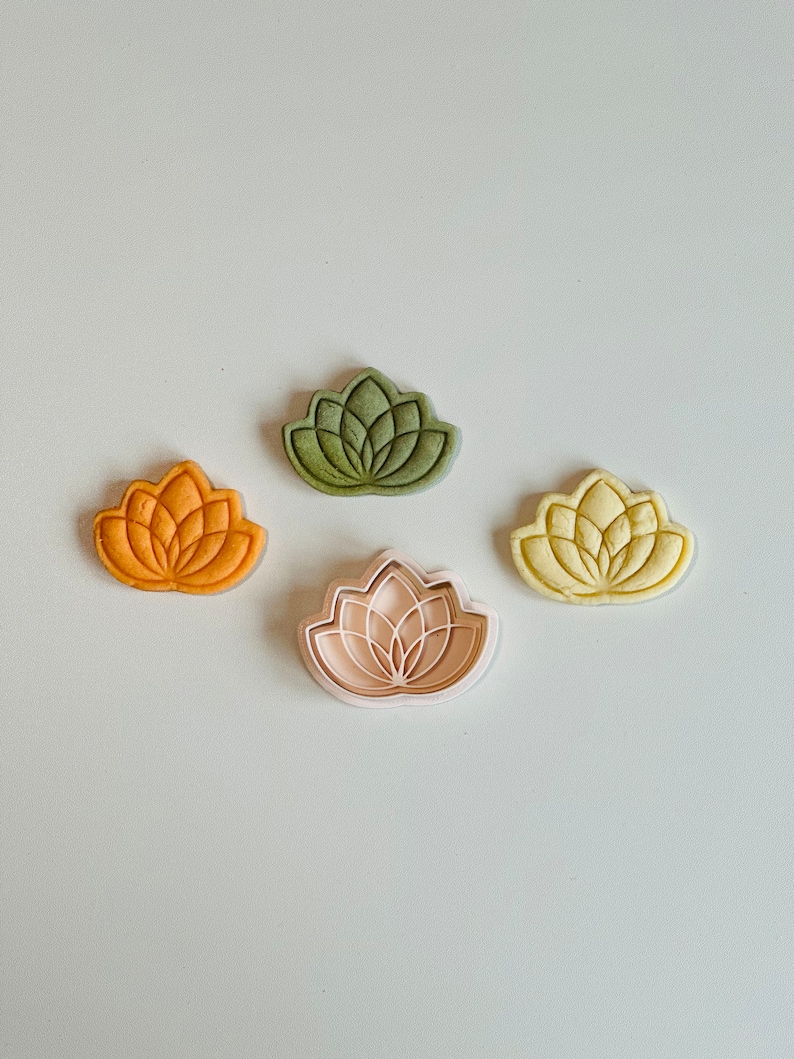May include: Four cookie cutters in the shape of a lotus flower. One cutter is green, one is yellow, one is orange, and one is pink.