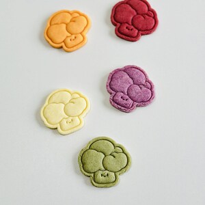 May include: Five colorful, cartoon-style mushroom-shaped cookies. The cookies are in shades of orange, red, purple, yellow, and green.