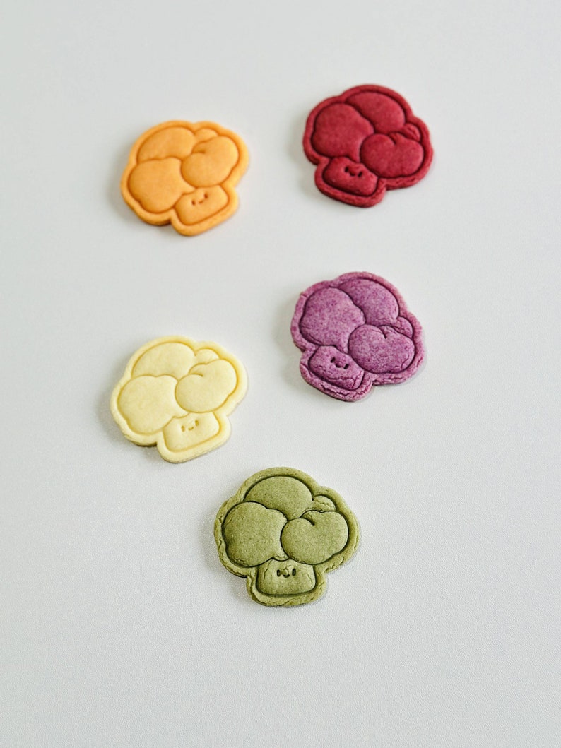 May include: Five colorful, cartoon-style mushroom-shaped cookies. The cookies are in shades of orange, red, purple, yellow, and green.