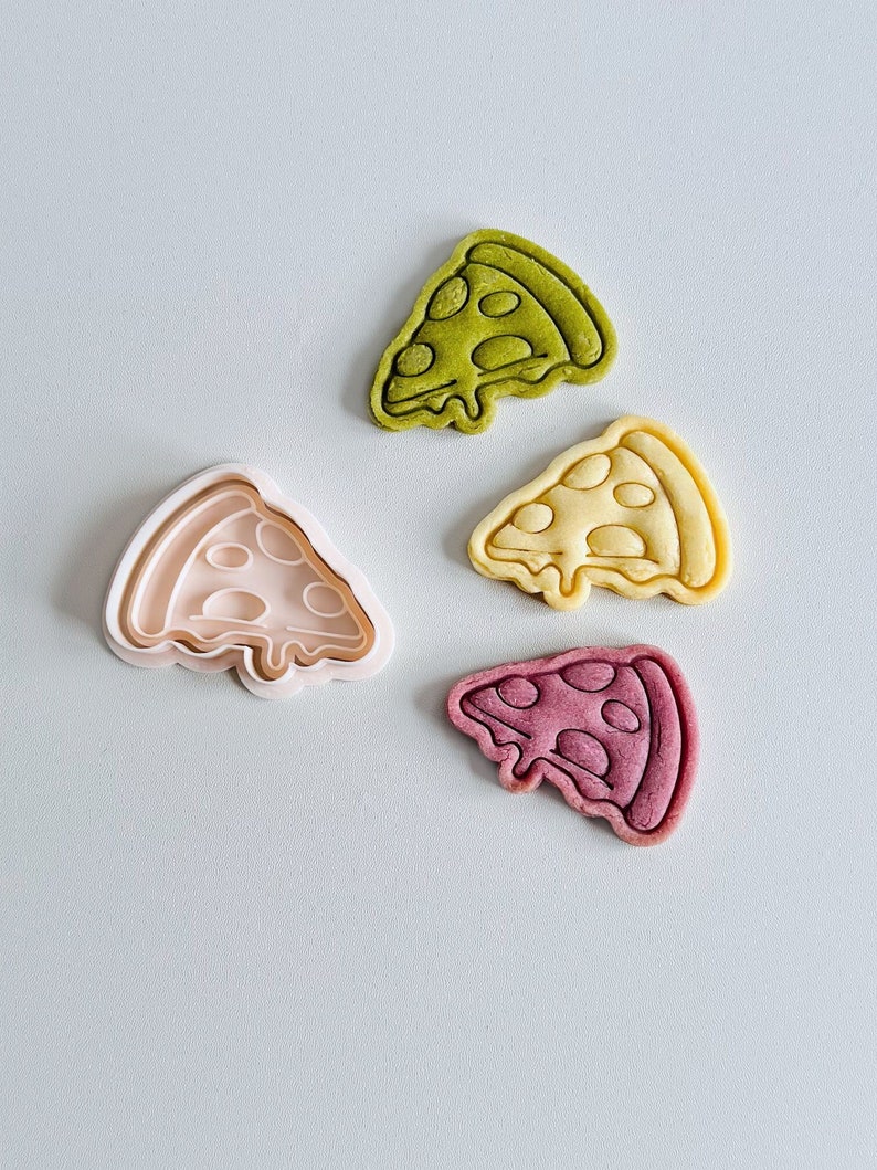 May include: Three cookie cutters in the shape of a pizza slice. The cutters are made of white plastic and are in different sizes. The largest cutter is open and the two smaller cutters are closed. The cutters are on a white surface.