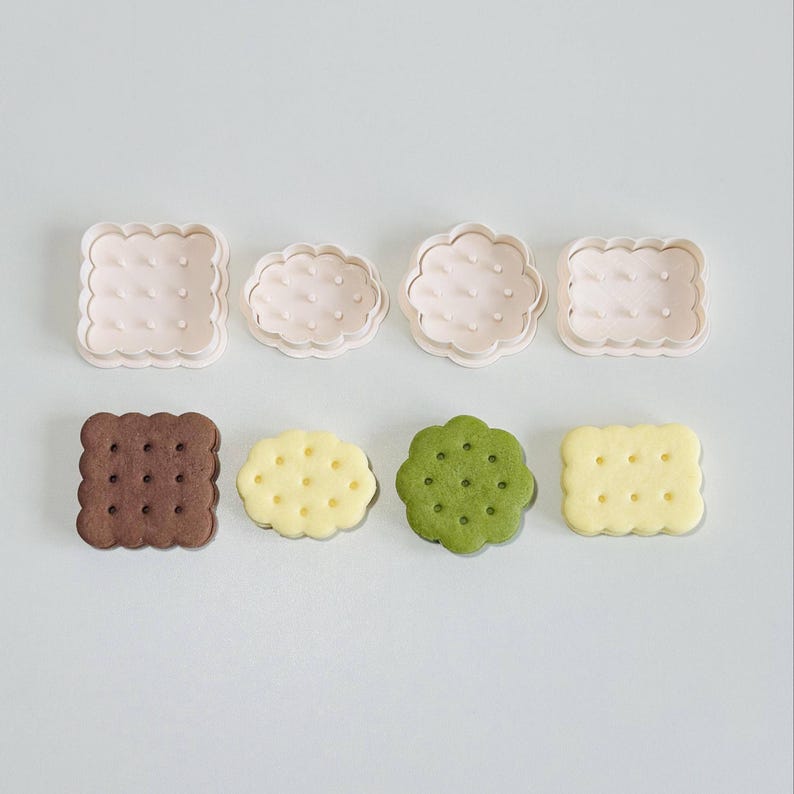 May include: Four cookie cutters in the shape of a square, a cloud, a circle, and a rectangle. Four cookies are shown, one each in brown, yellow, green, and white.
