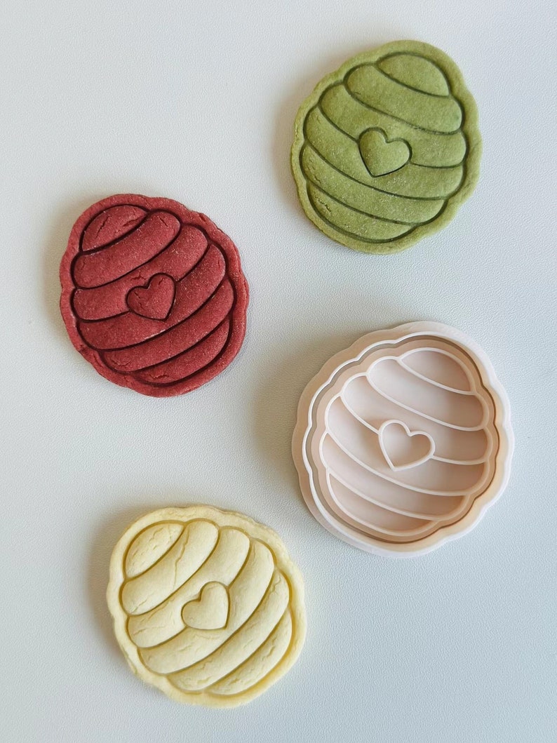 Pu&ograve; includere: Tre stampini per biscotti a forma di favo con un cuore al centro. Gli stampini sono verde, rosso e giallo. Gli stampini sono su uno sfondo grigio chiaro.