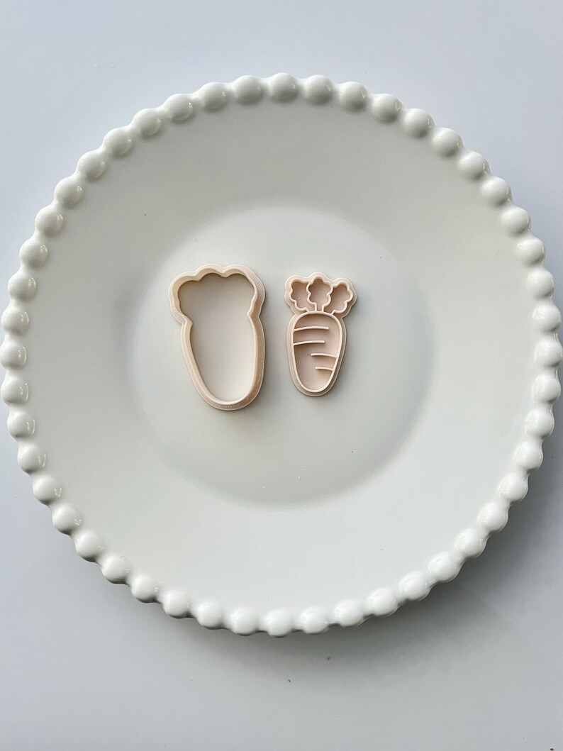 May include: Two plastic cookie cutters, one shaped like a carrot and the other shaped like a leaf. The carrot cutter has a green top and orange body with lines.
