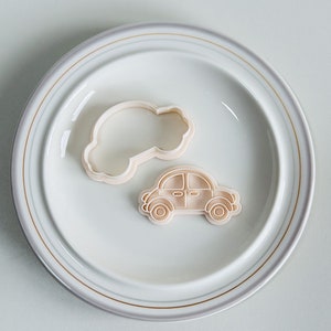 May include: Two plastic cookie cutters on a white plate with a gold rim. One cutter is shaped like a car and the other is shaped like a cloud.