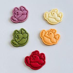 Op de afbeelding: Vijf koekjes in de vorm van kuikens in verschillende kleuren: paars, geel, groen, oranje en rood. Elk koekje heeft een gedetailleerde omtrek en gezichtskenmerken. Deze koekjes zijn waarschijnlijk zelfgemaakt en geschikt voor een lente- of Paasthema.