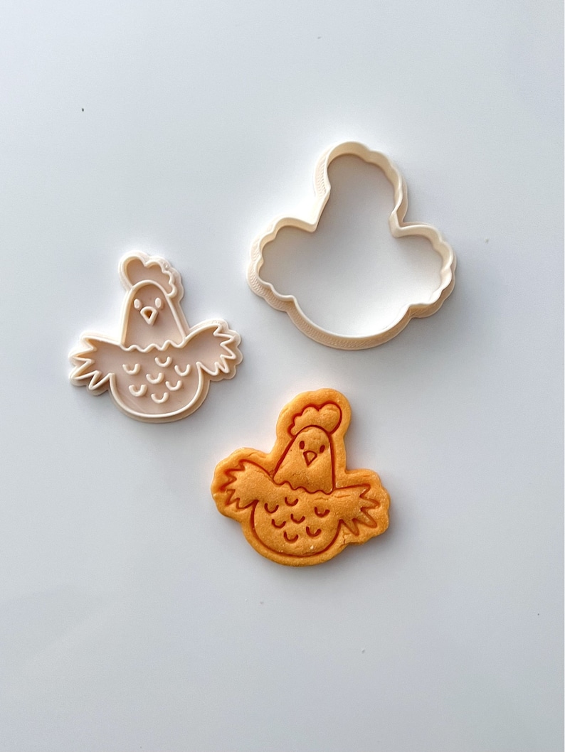 May include: A white plastic cookie cutter and a yellow cookie in the shape of a cartoon chicken.