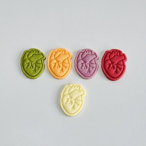 May include: Five heart-shaped cookies in different colors: green, orange, purple, red, and white. The cookies are arranged in a semi-circle with the white cookie at the bottom.