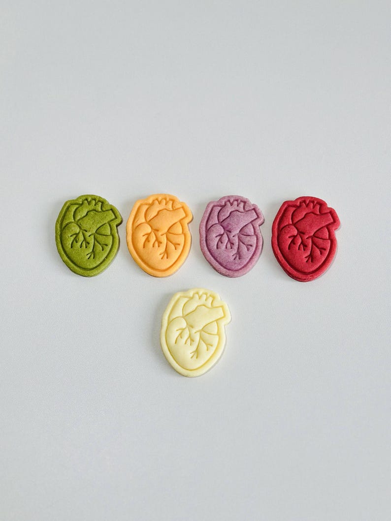May include: Five heart-shaped cookies in different colors: green, orange, purple, red, and white. The cookies are arranged in a semi-circle with the white cookie at the bottom.