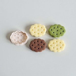 May include: Five cookie cutters in the shape of clouds. One cutter is pink and the other four are white. The white cutters have small holes throughout the shape.