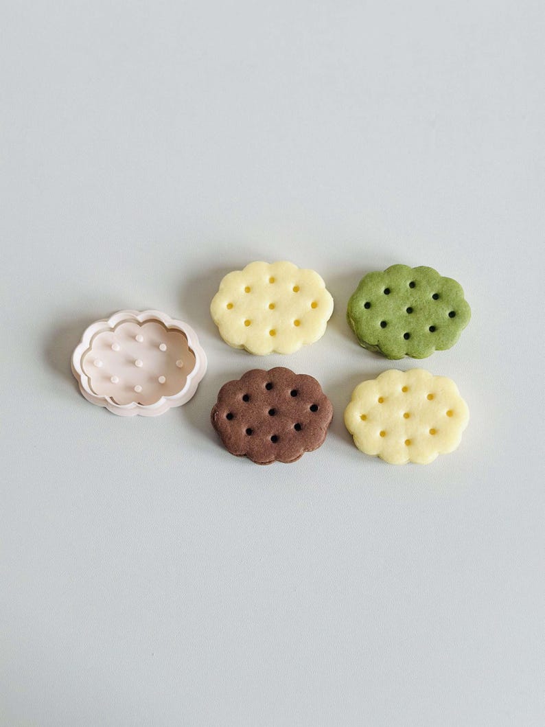 May include: Five cookie cutters in the shape of clouds. One cutter is pink and the other four are white. The white cutters have small holes throughout the shape.