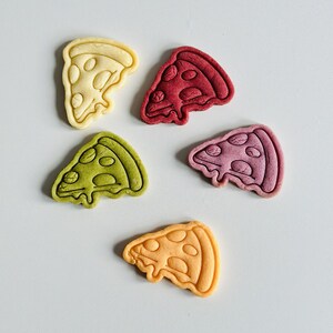 May include: Five pizza-shaped cookies in different colors: yellow, red, green, orange, and purple. The cookies are arranged on a white surface.