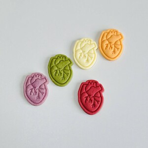 May include: Five heart-shaped cookies in different colors: purple, green, yellow, orange, and red. The cookies are arranged in a semi-circle on a white background.