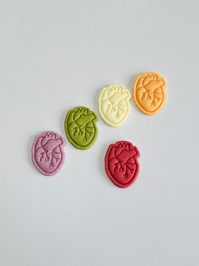May include: Five heart-shaped cookies in different colors: purple, green, yellow, orange, and red. The cookies are arranged in a semi-circle on a white background.