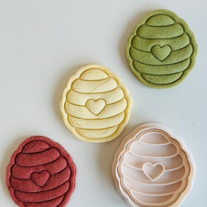 Pu&ograve; includere: Quattro stampini per biscotti a forma di alveare con un cuore al centro. Gli stampini sono di diversi colori: verde, giallo, marrone e bianco.