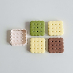 May include: Four square-shaped cookies, two yellow, one green, and one brown, with a plastic cookie cutter in the shape of a square with rounded edges.