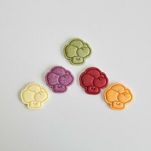 May include: Five colorful broccoli-shaped cookies with happy faces. The cookies are green, purple, red, yellow, and white.