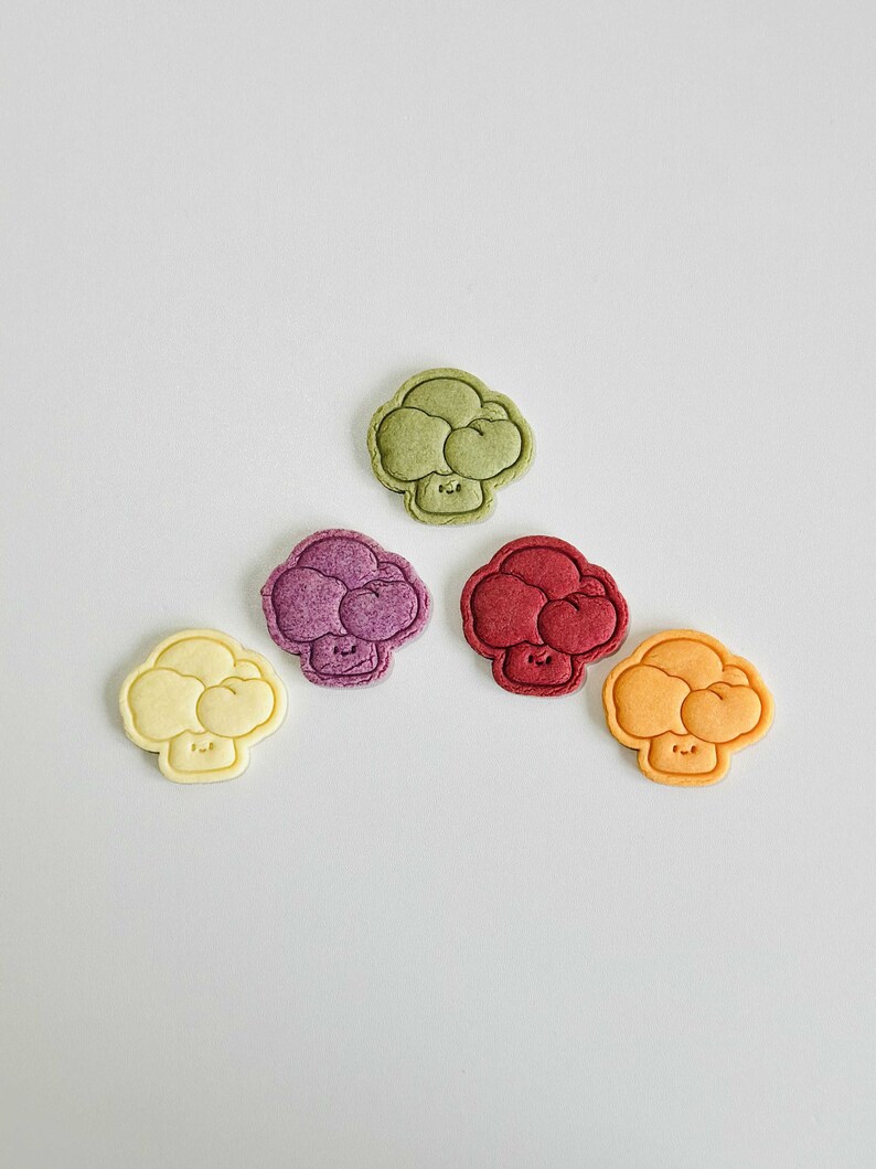 May include: Five colorful broccoli-shaped cookies with happy faces. The cookies are green, purple, red, yellow, and white.