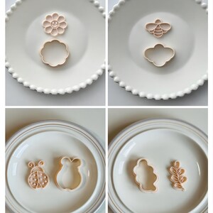 May include: Four white plates with different cookie cutters on them. The cutters are shaped like a flower, a bee, a ladybug, a cloud, a bear, and a leaf.