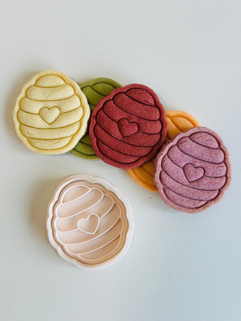 Pu&ograve; includere: Quattro stampini per biscotti colorati a forma di favo con un cuore al centro. Gli stampini per biscotti sono disposti in cerchio con uno stampino per biscotti bianco al centro.