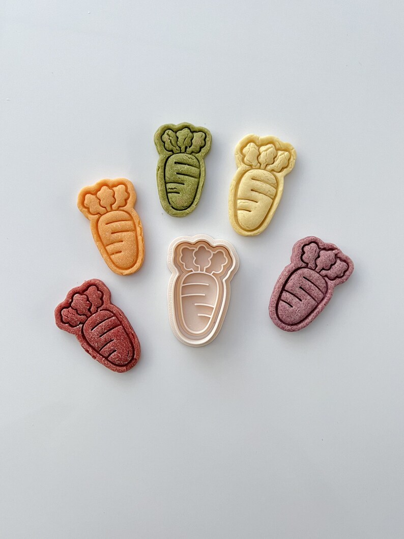 May include: Six carrot-shaped cookie cutters in various colors, including green, yellow, orange, and red. One of the cutters is white and appears to be made of plastic.