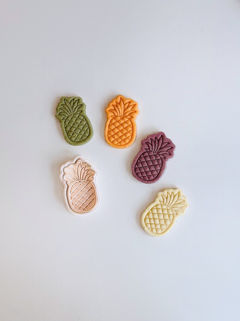 May include: Five pineapple-shaped cookie cutters in different colors: green, orange, purple, pink, and yellow.