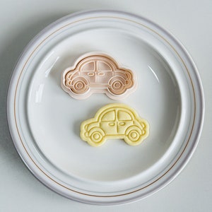 May include: Two cookie cutters in the shape of a car. The top cutter is pink and the bottom cutter is yellow.