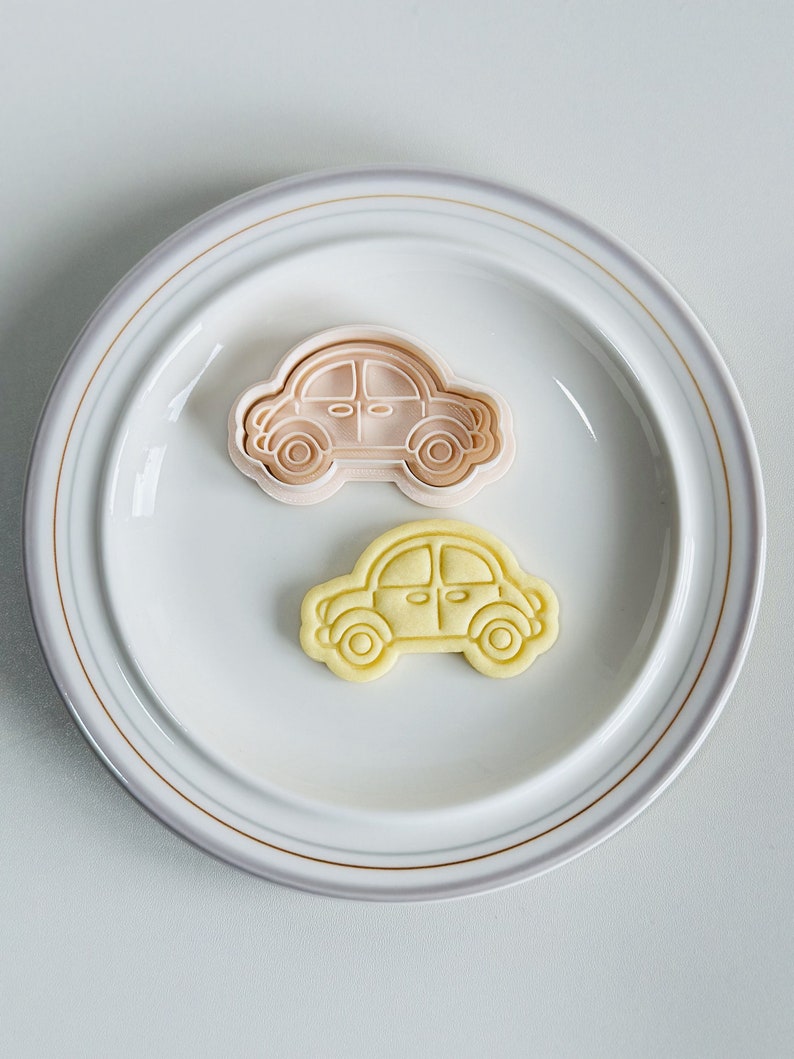 May include: Two cookie cutters in the shape of a car. The top cutter is pink and the bottom cutter is yellow.