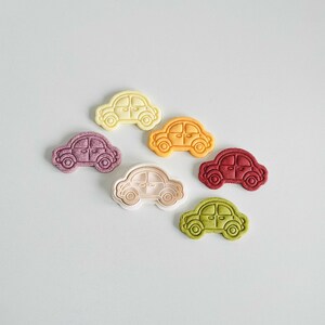 May include: Six cookie cutters shaped like cars in different colors: white, yellow, purple, white, red, and green.