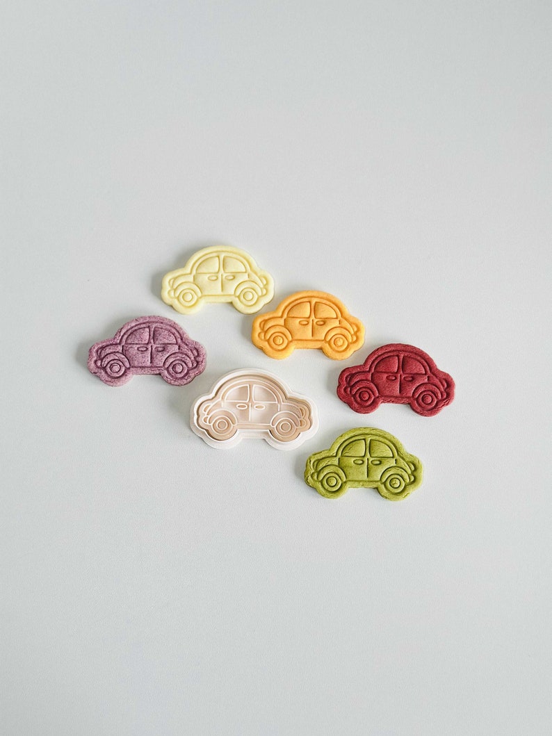 May include: Six cookie cutters shaped like cars in different colors: white, yellow, purple, white, red, and green.
