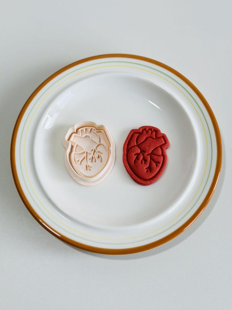 May include: Two heart-shaped cookie cutters, one pink and one red, on a white plate with a brown rim.
