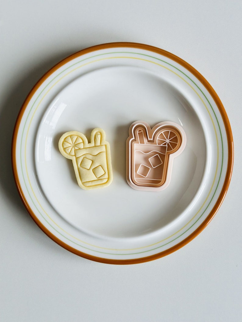 Pu&ograve; includere: Due stampini per biscotti, uno giallo e uno rosa, a forma di bicchieri di t&egrave; freddo con limoni e cannucce.
