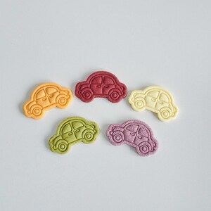 May include: Five small car-shaped cookies in different colors: red, orange, yellow, green, and purple.