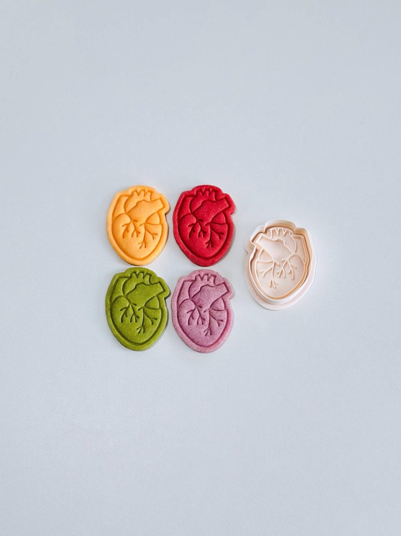 May include: Five heart-shaped cookie cutters, four are red, green, yellow, and pink, and one is a clear plastic cutter.