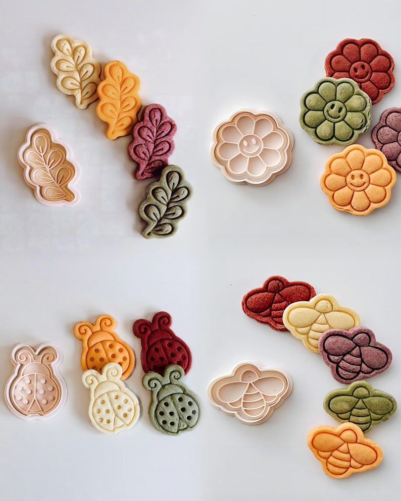 May include: Assortment of cookie cutters and cookies in various shapes and colors. The cookie cutters include a flower, a ladybug, and a bee. The cookies are in the shapes of a flower, a ladybug, and a bee. The cookies are in various colors, including red, green, yellow, and orange.