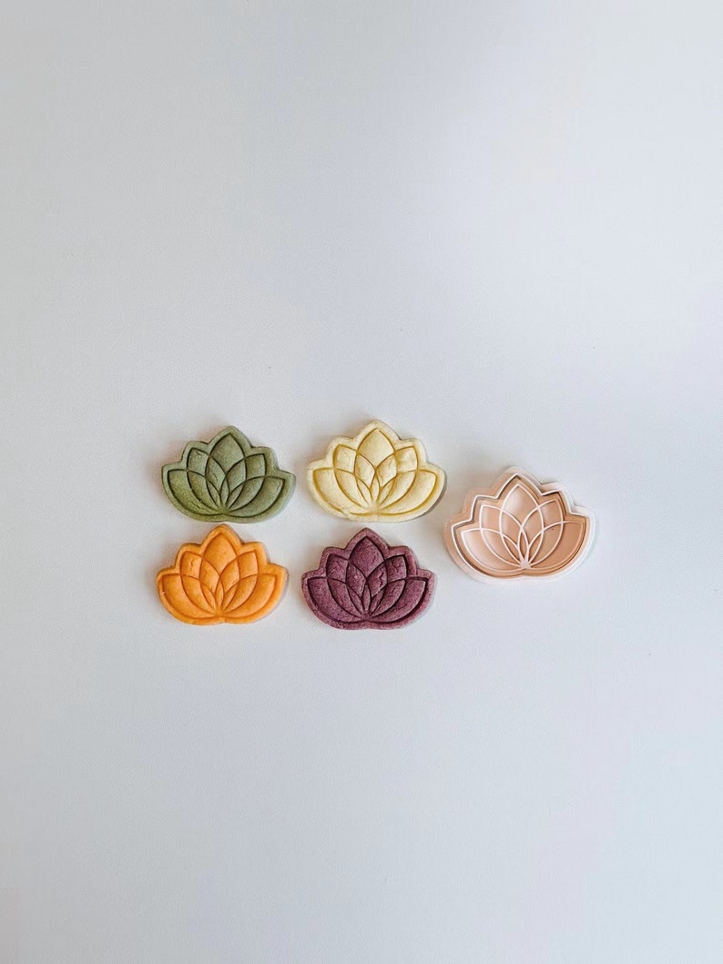 May include: Five different colored cookie cutters shaped like a lotus flower. The cutters are green, yellow, orange, purple, and pink.