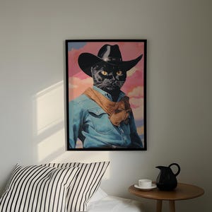a framed picture of a black cat wearing a cowboy hat and a blue denim shirt, hanging on a wall above a bed with a striped pillow.