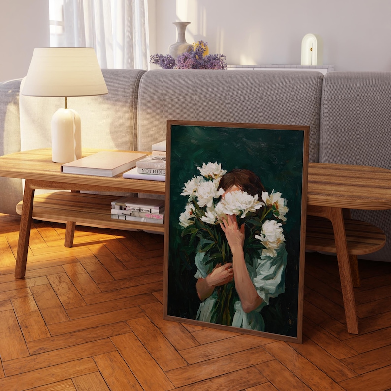 a painting of a woman holding a bouquet of white flowers, with her face partially obscured by the flowers. The painting is displayed on a wooden table in a living room setting, with a lamp and other decorative items visible in the background.
