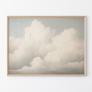 May include: A framed print of a painting depicting a cloudy sky. The clouds are white and grey, and the sky is a light blue. The painting is framed in a light wood frame.