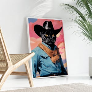 A framed poster of a black cat wearing a cowboy hat and blue denim jacket, standing on a white floor next to a woven chair.