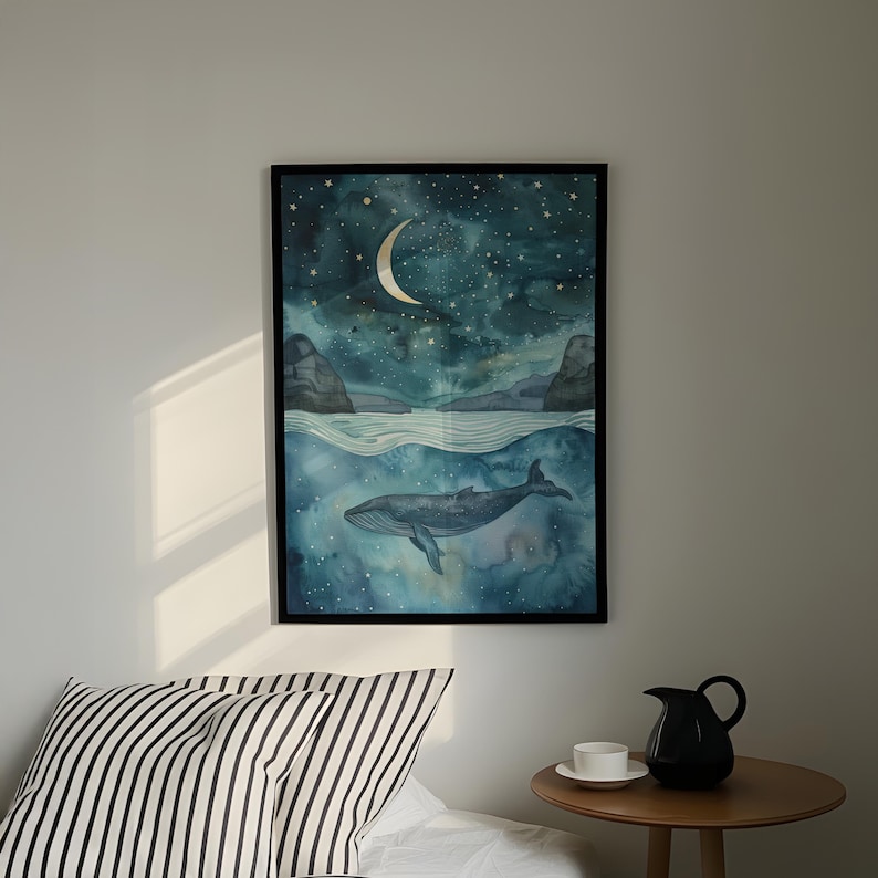 a framed painting of a whale swimming in the ocean under a starry night sky, hanging on a wall above a bed with a striped pillow.