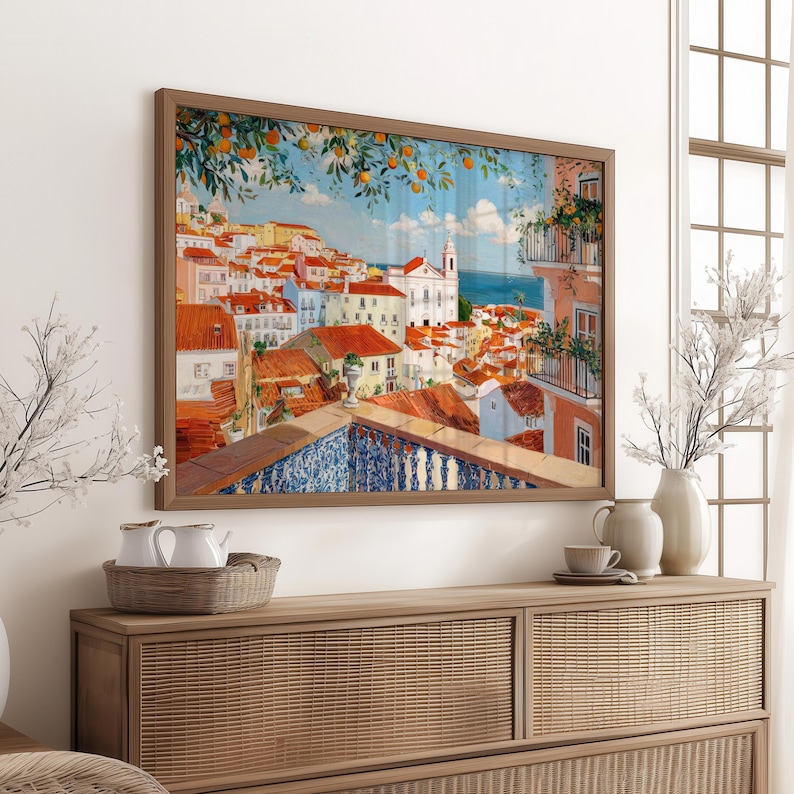 a large framed painting of a colorful cityscape with buildings, balconies, and trees, hanging on a wall above a wooden dresser.