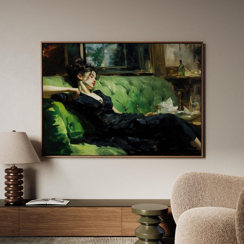a woman in a black dress sitting on a green couch, with a lamp and a book on a side table in front of her.