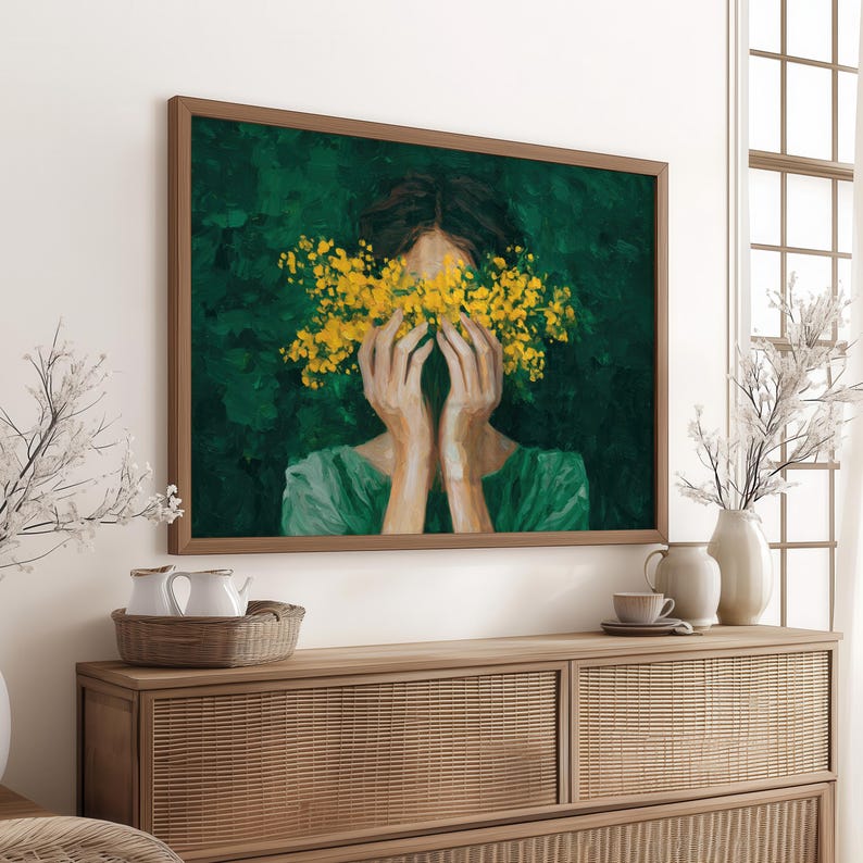 a large painting of a woman with her hands covering her face, surrounded by yellow flowers. The painting is displayed on a wall above a wooden dresser, which has various decorative items such as a vase, a teapot, and a bowl.