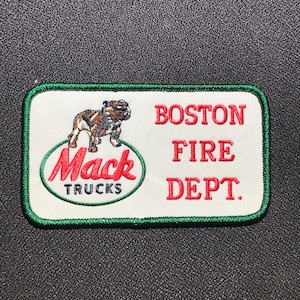 Może przedstawiać: Biała łatka z zieloną obwódką. Łatka przedstawia czerwonego buldoga, zielone logo Mack Trucks i napis "BOSTON FIRE DEPT."